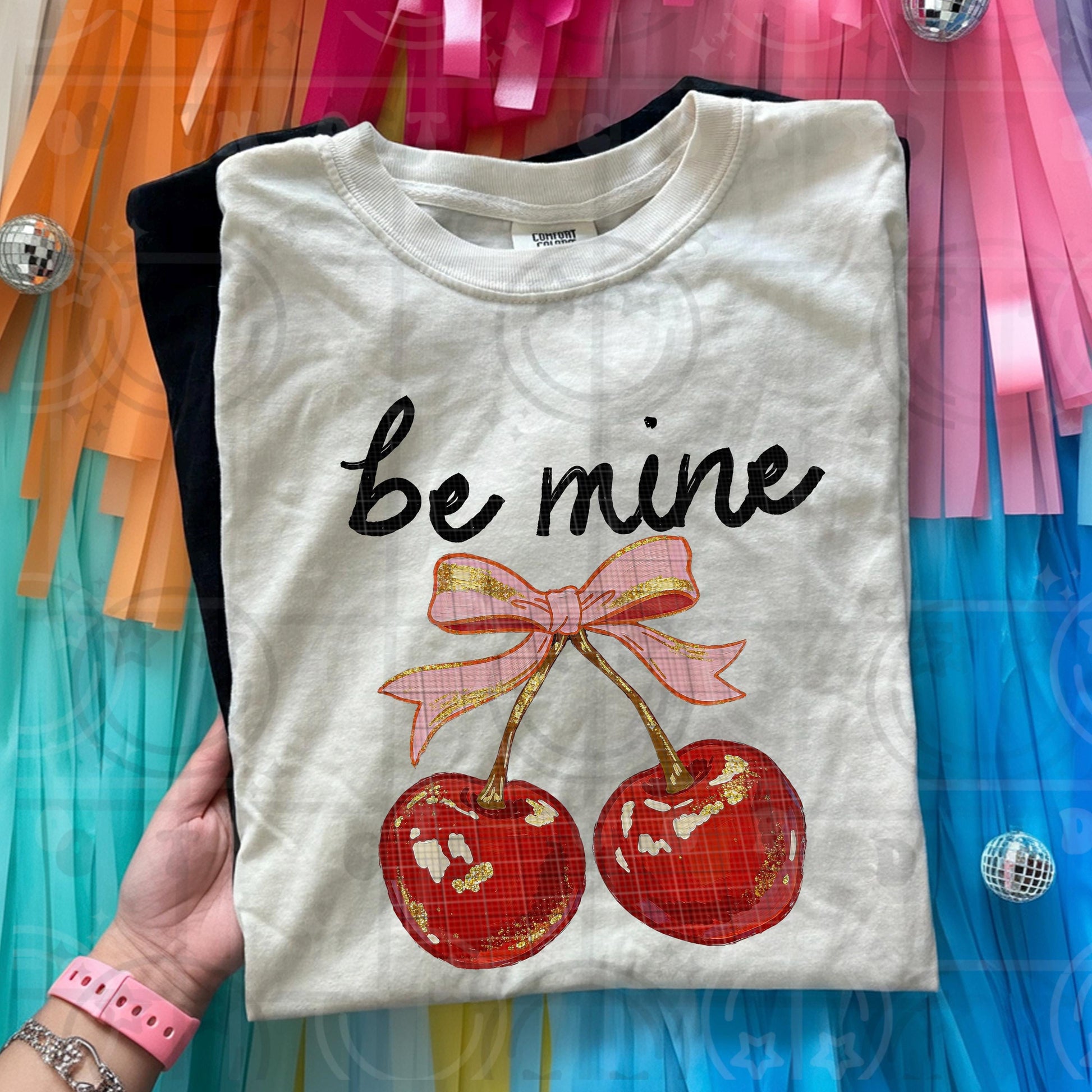 Retro Be Mine Valentine cherry design with red cherries and pink bow featuring wavy lettering vintage inspired texture and playful Valentine aesthetic shown on light shirt background